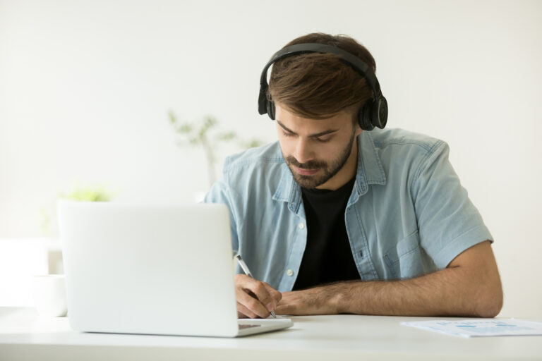 Junger Mann mit Kopfhörern lernt Deutsch am Laptop