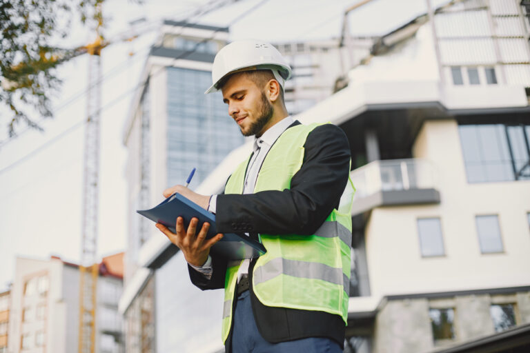 Ingenieur mit Schutzhelm und Warnweste macht sich Notizen auf einer Baustelle