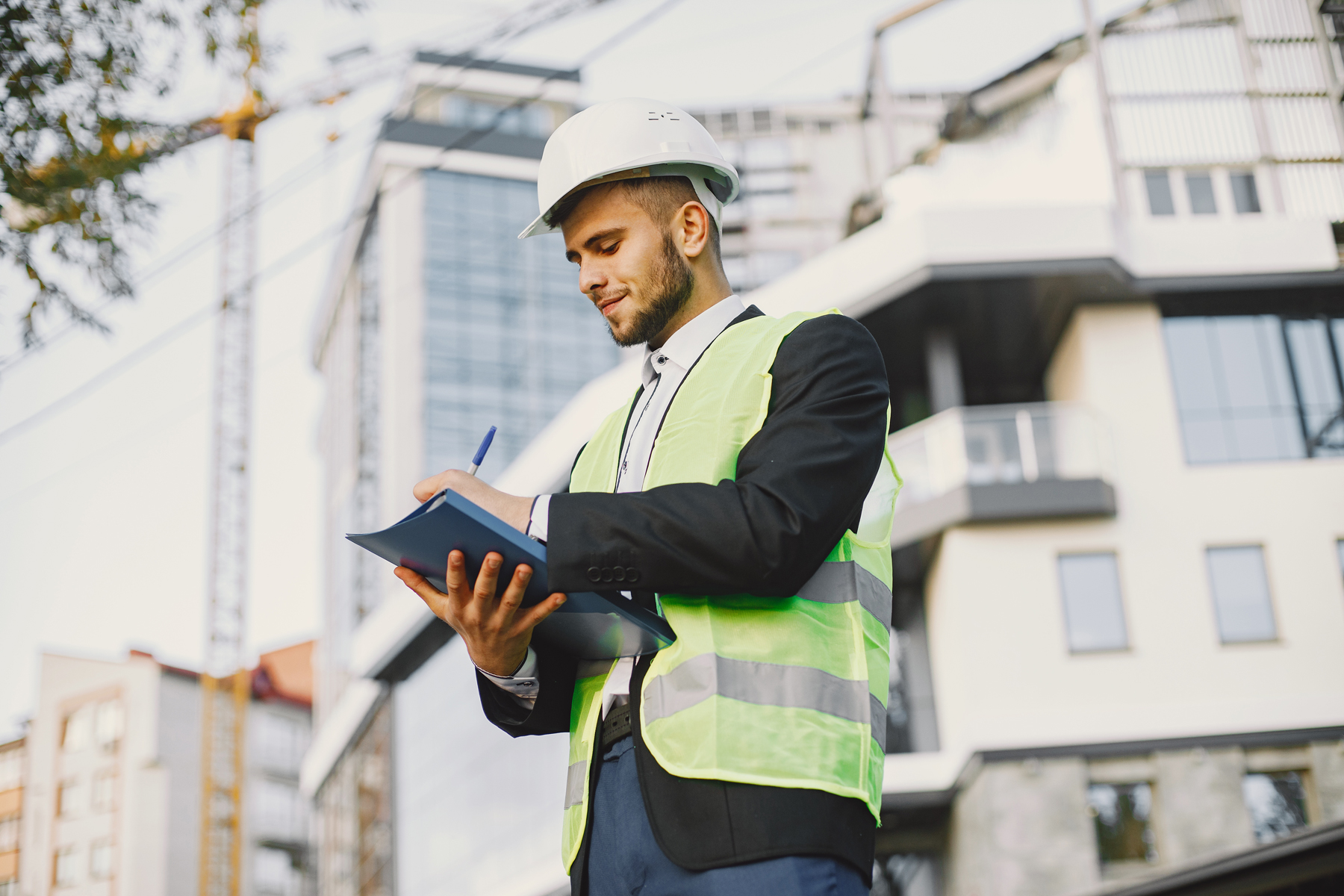 Ingenieur mit Schutzhelm und Warnweste macht sich Notizen auf einer Baustelle
